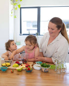 Woman and two children at a kitchen table with food and drinks.