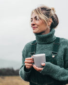 Woman holding a mug outdoors with a neutral background.