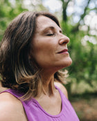 Woman in a purple tank top with a blurred green background.