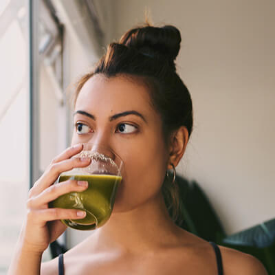 Woman drinking green juice indoors.