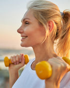 Blonde woman lifting yellow weights against a blurred background.