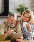 Woman and man smiling over a tablet in a kitchen.