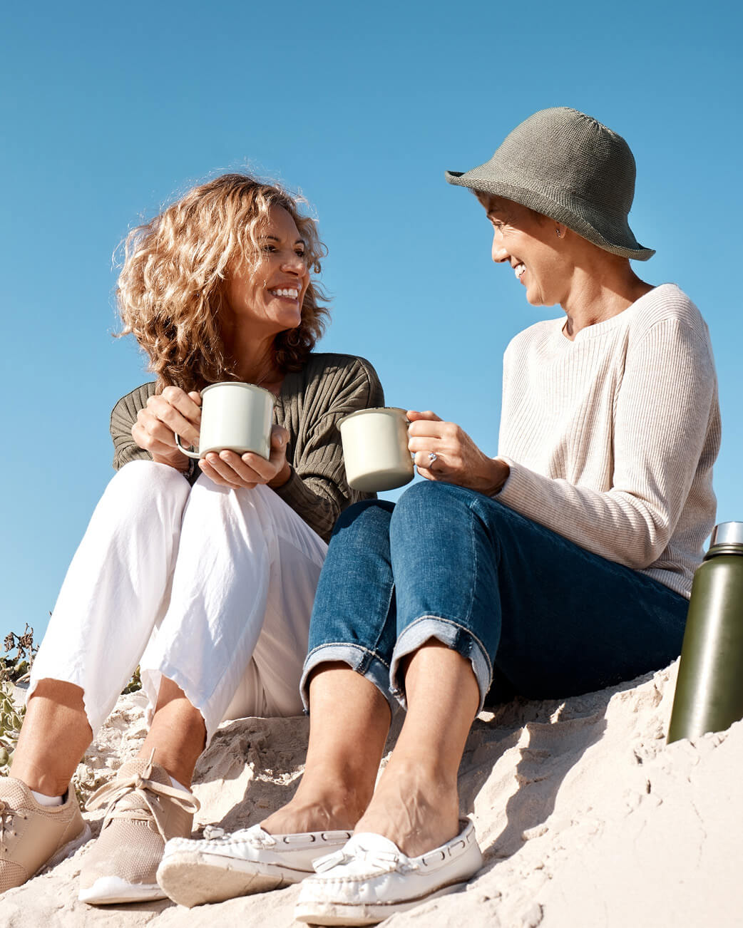Two women drinking out of mugs against a blue sky.