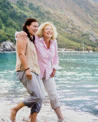 Two woman laughing while walking along a beach with mountains in the background.