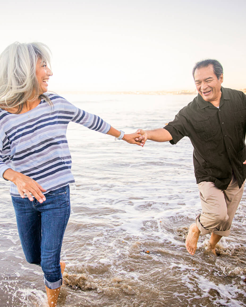 Woman and man running in the water at the beach.