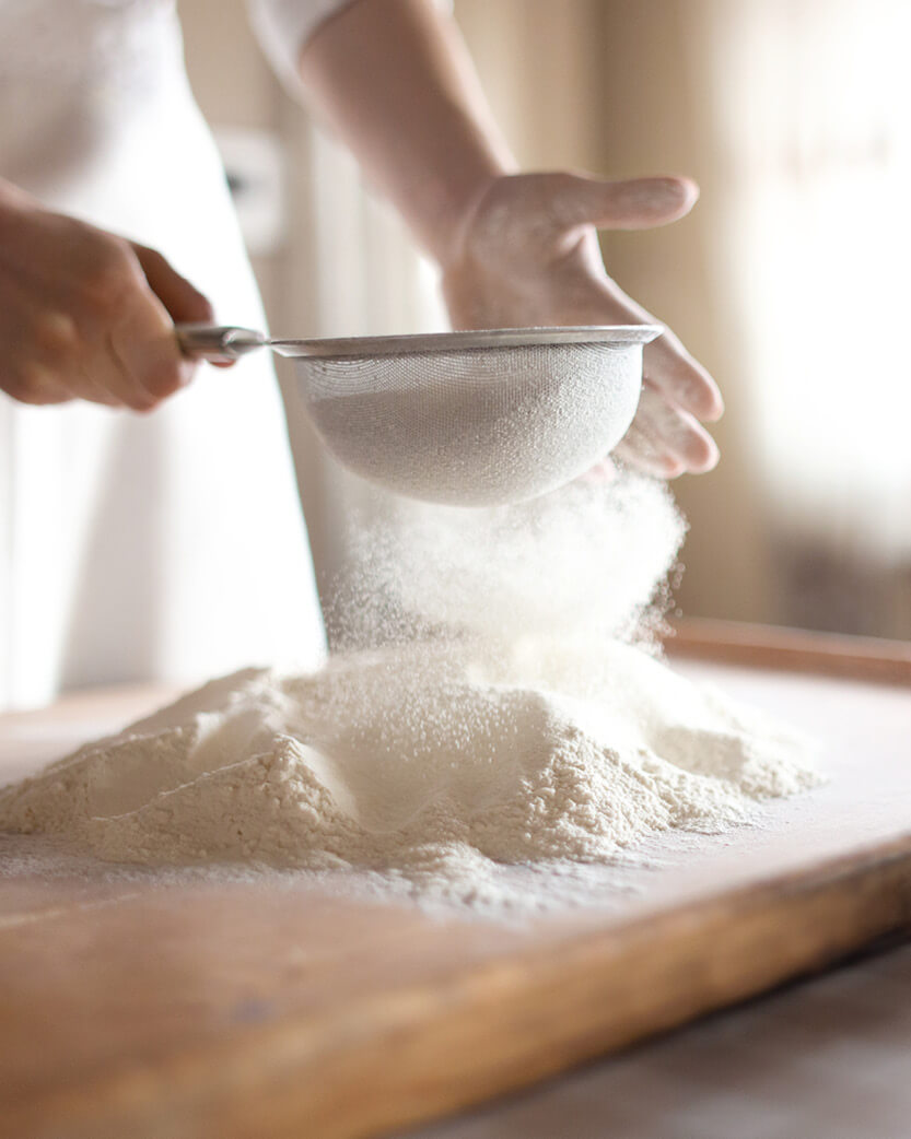 Person sifting flour into a bowl on a wooden surface