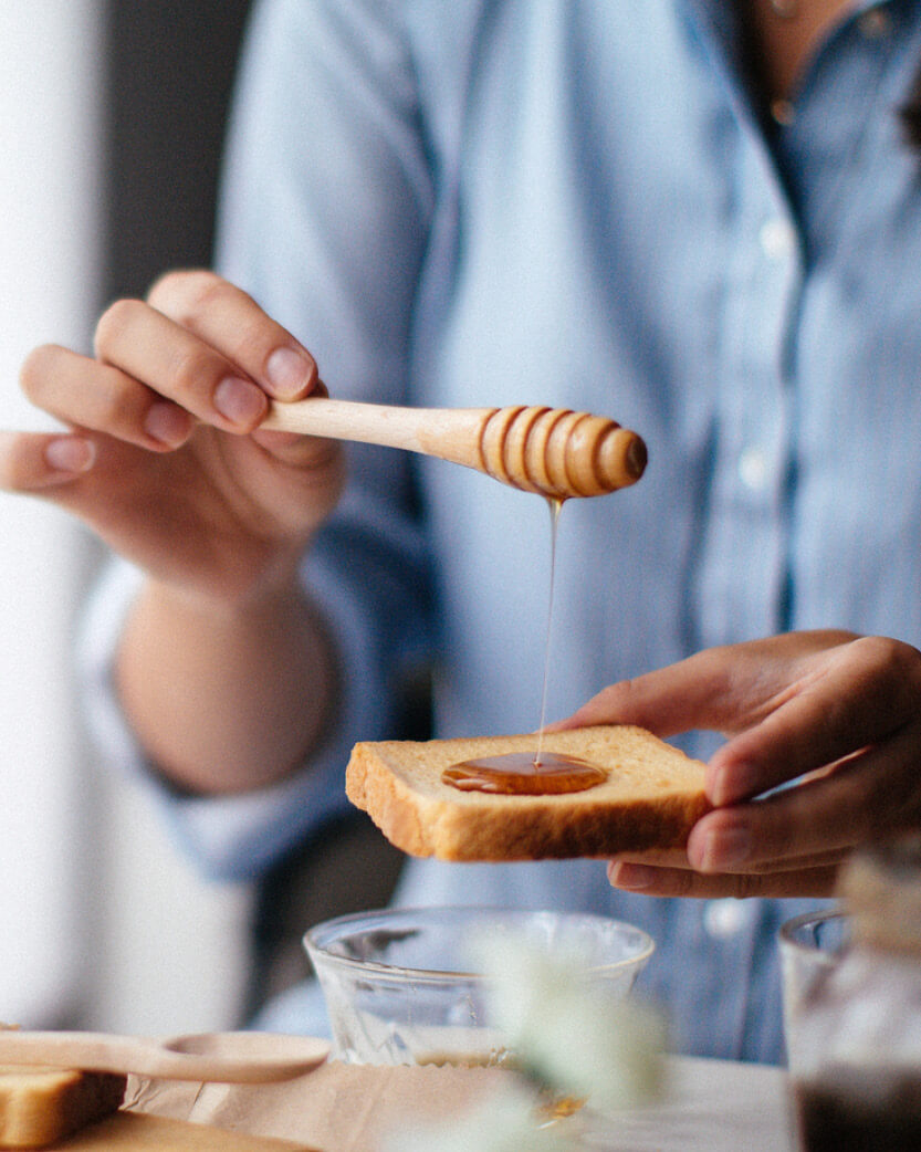 Person drizzling honey from a wooden dipper onto toast