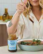Person pouring beef bone broth into a bowl of soup with kale.