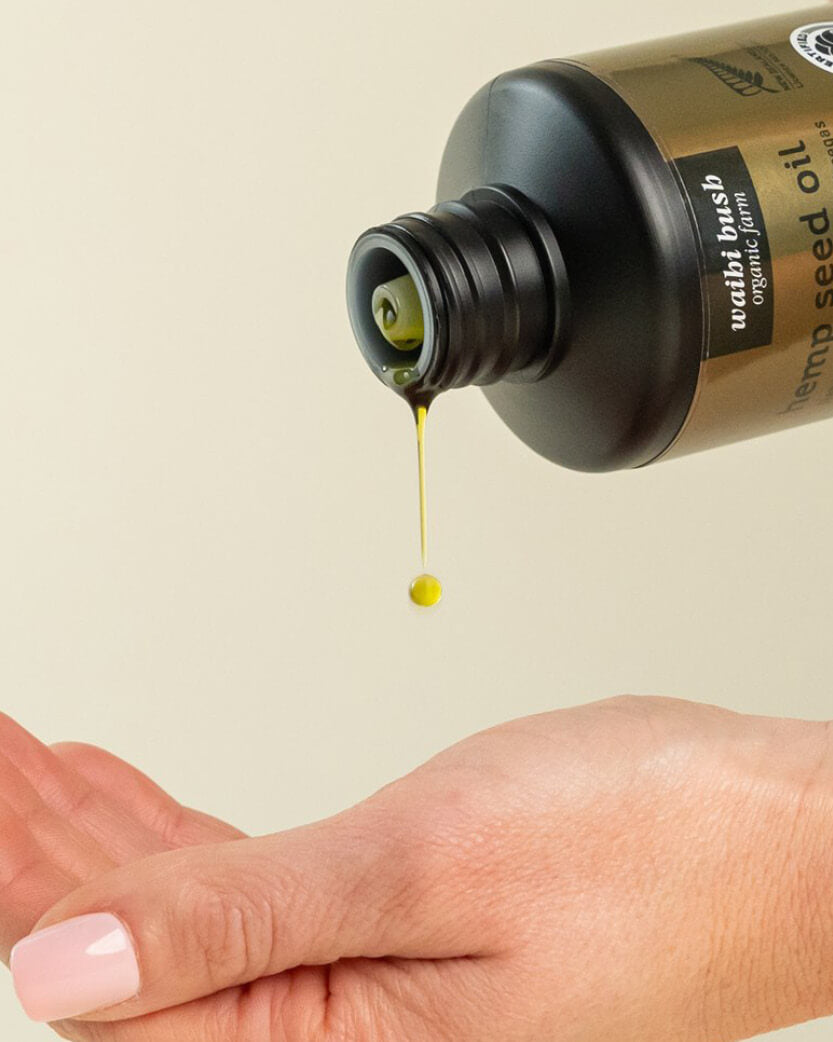 Hand holding a bottle of Wahi Organic Hemp Seed Oil with oil dripping onto skin.