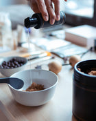 Hand pouring a liquid from a bottle into a bowl on a kitchen counter.