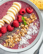 Berry smoothie bowl with banana, raspberries, granola, and coconut in a grey bowl.