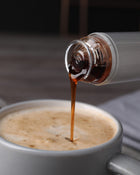 Bottle of syrup being poured into a cup of coffee