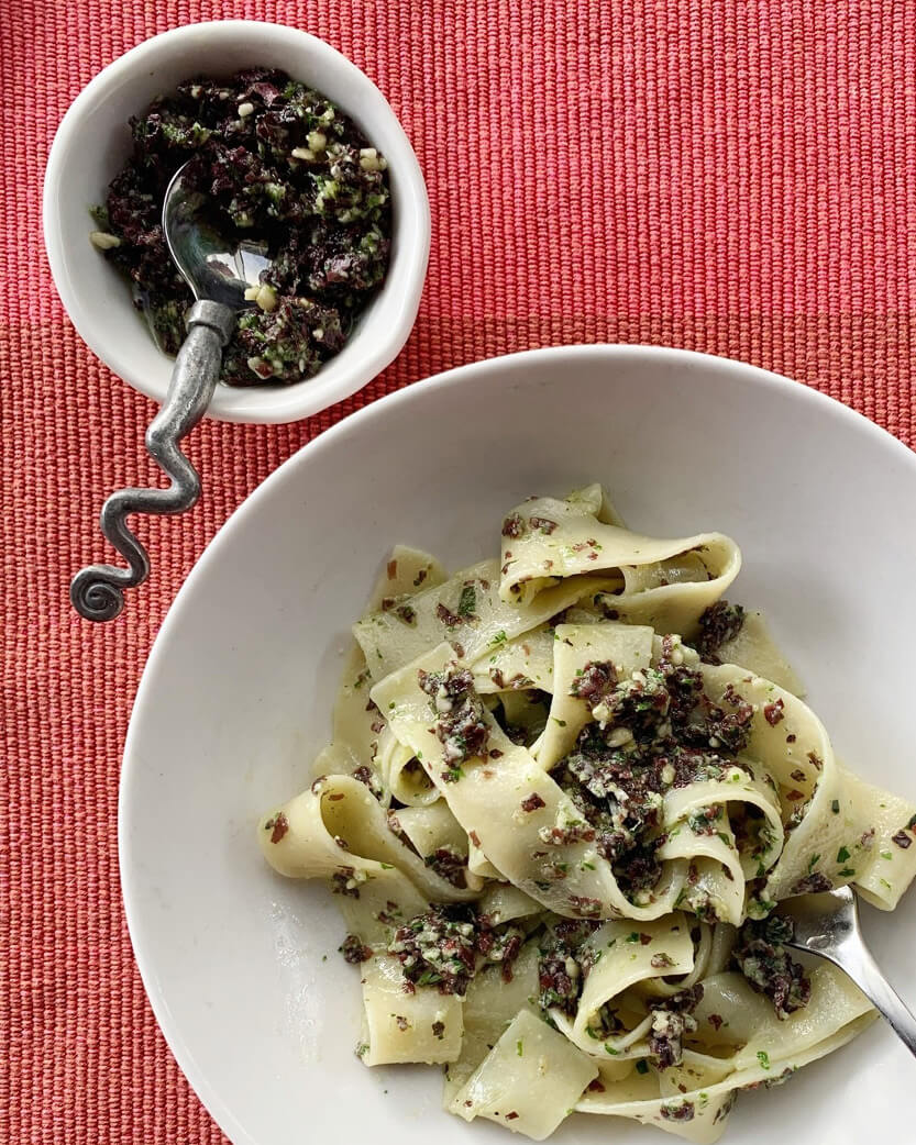 Pasta dish with a side of dark green seaweed sauce on a red textured surface
