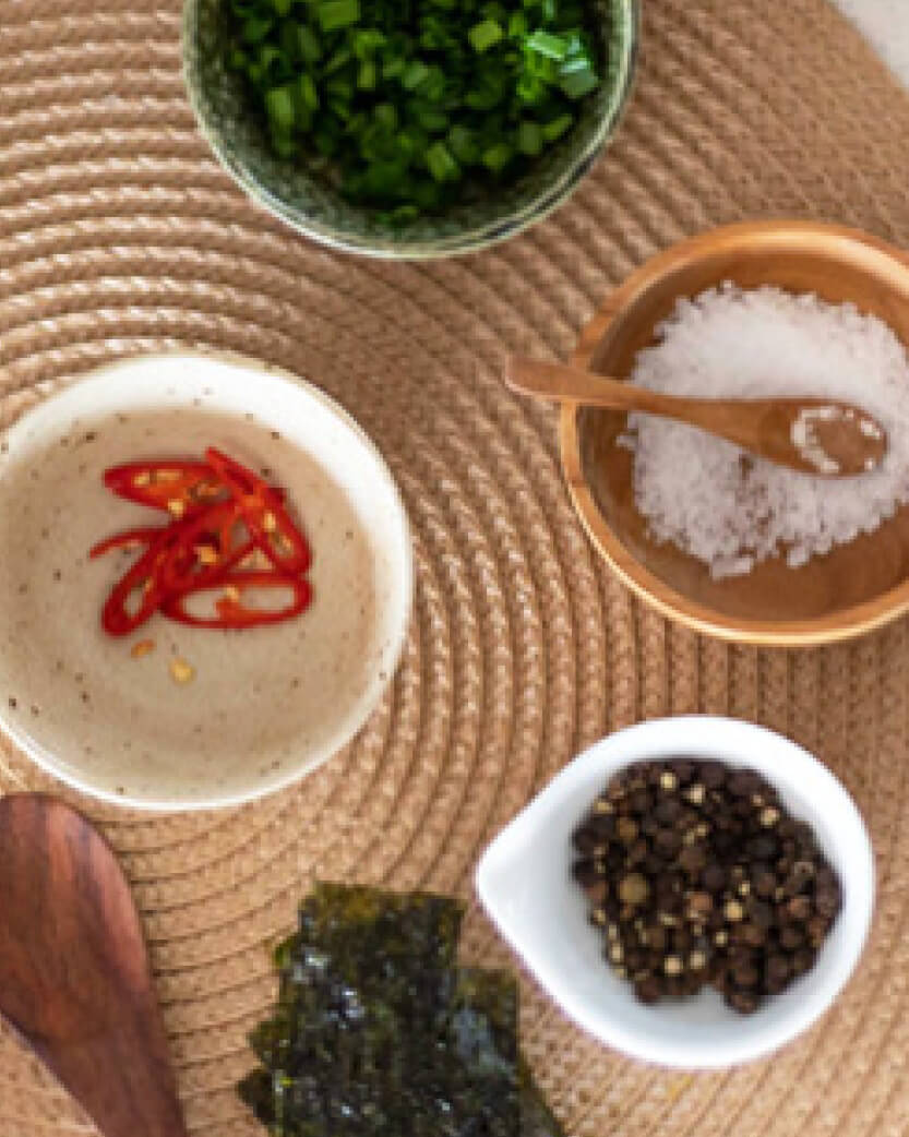 Assorted ingredients including red chili peppers, seaweed, and salt on a woven mat.