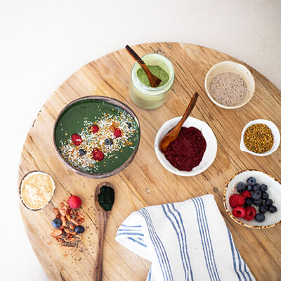 Green smoothie bowl with toppings on a wooden board.
