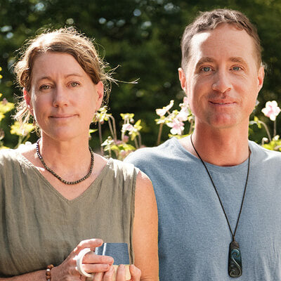 Two people standing outdoors with a blurred natural background.