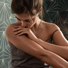 Woman embracing herself against a geometric-patterned wall.