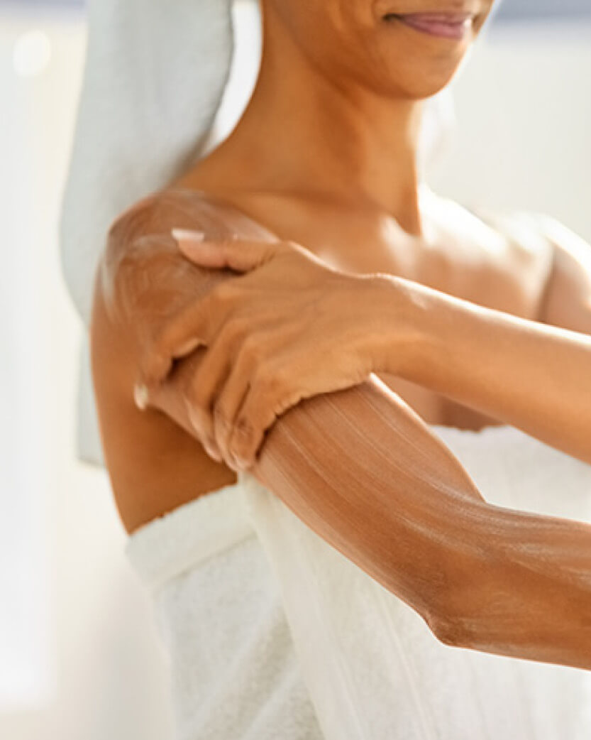 Person applying lotion to their arm with a blurred background.