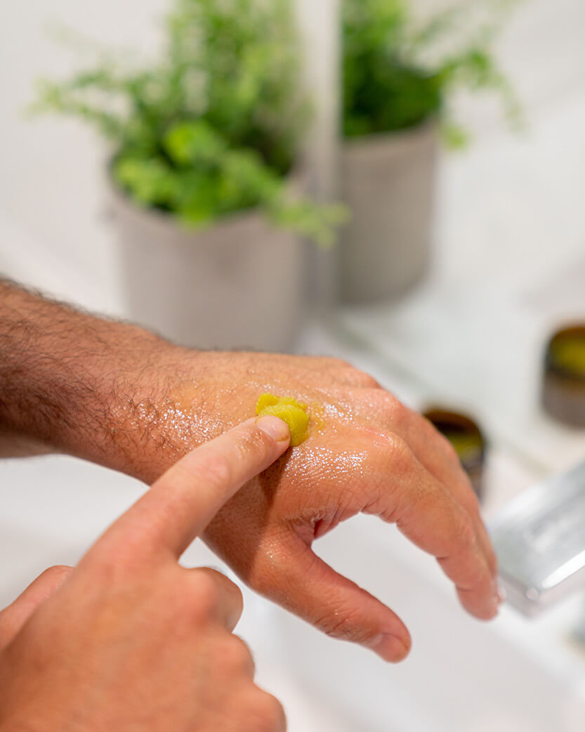 Person applying a green gel to their hand with plants in the background.