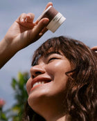 Person applying sunscreen to a woman's face outdoors.
