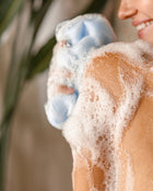 Person washing with a blue bar of soap on a soapy hand against a blurred natural background.