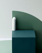 Green & blue geometric wall art with a white cylindrical object on a light gray background.