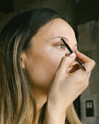 Side view of woman using an eyebrow pencil on their face.