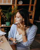 Woman applying facial mask in a home setting.