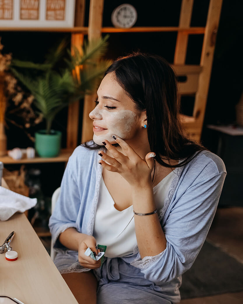 Woman applying facial mask in a home setting.