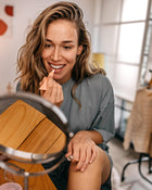 Woman applying lip balm in front of a mirror indoors.