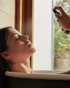 Person applying sunscreen to a woman's face by a window.