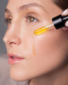 Close-up of a woman applying a dropper of skincare product to her face.