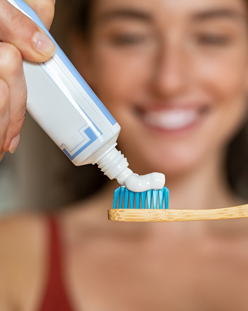 Person applying toothpaste to a toothbrush with a blurred background.