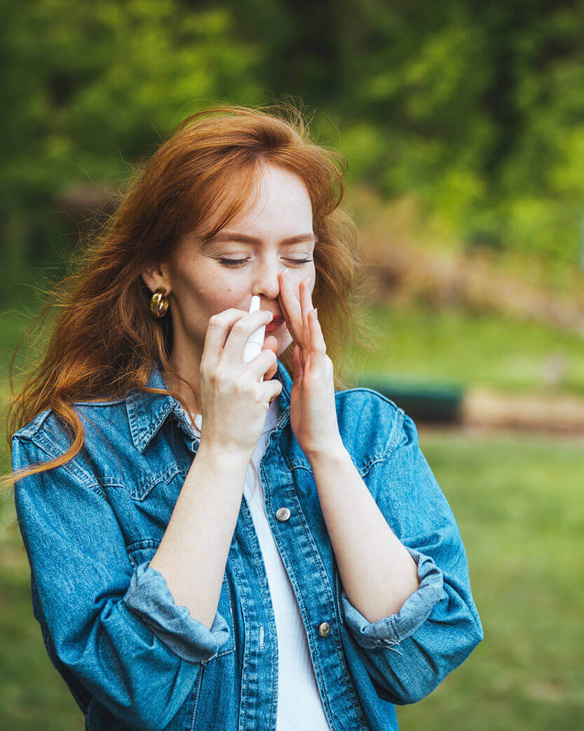 Woman in a denim jacket covering her mouth with her hands outdoors.
