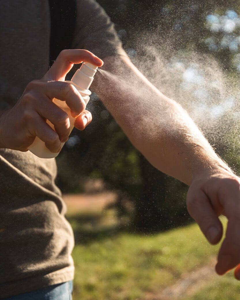 Person applying a spray to their arm outdoors.