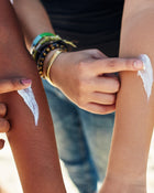 Person applying sunscreen to another person's arm on a beach.