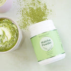 BioBalance Matcha Powder container next to a matcha latte on a white surface.