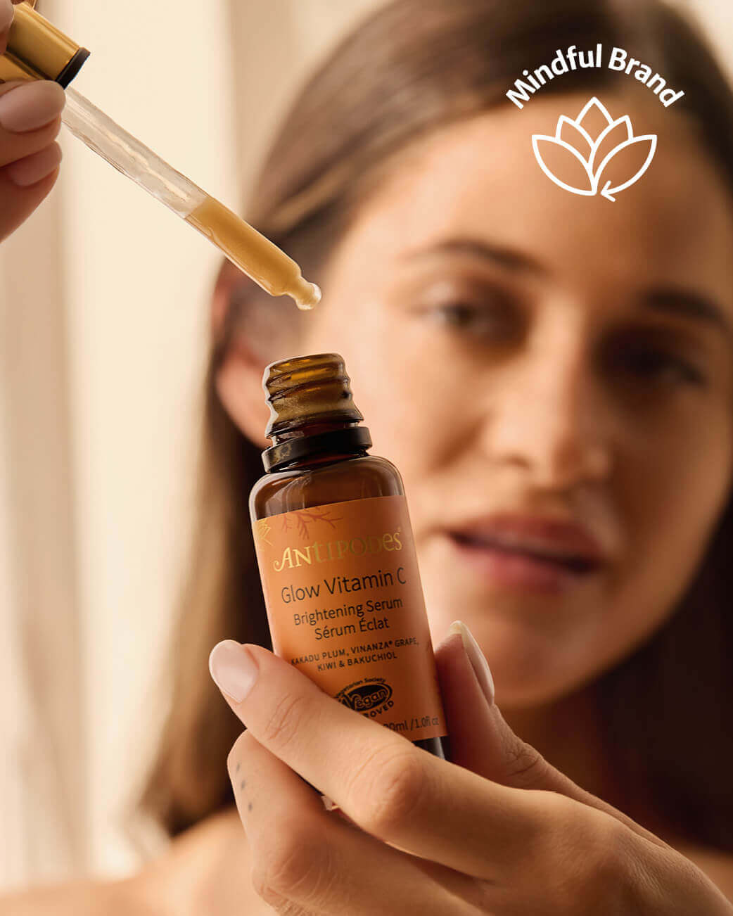 Person holding a bottle of Antipodes Vitamin C serum with a Mindful Brand logo in the corner.