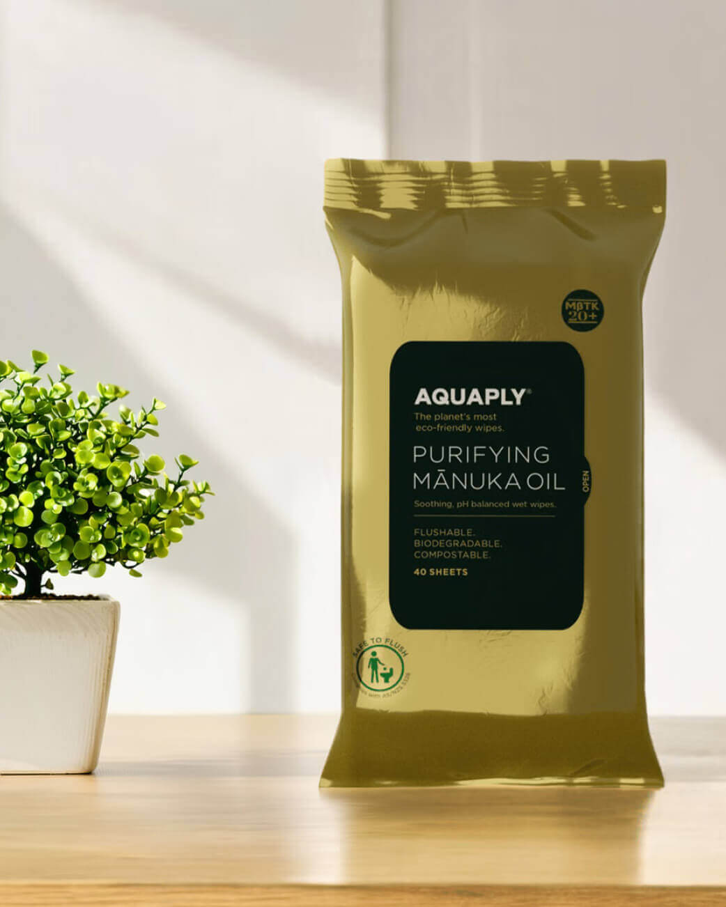 Pack of Aquaply Purifying Manuka Oil wipes on a wooden surface with a plant in the background.