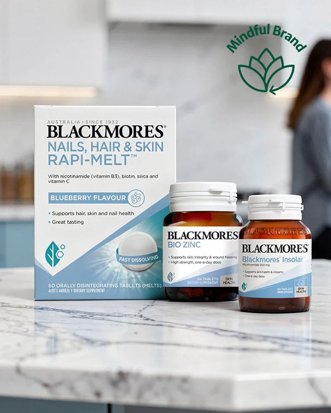 Blackmores Nails, Hair & Skin Rapi-Melt blueberry flavour tablets shown with its retail box and two supplement bottles on a marble countertop. A blurred person is visible in the background, and a 'Mindful Brand' logo appears in the top right.