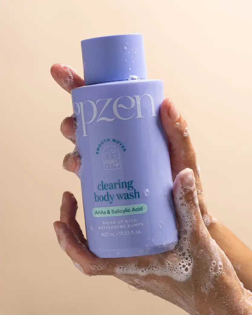 Hand holding a blue bottle of Epzen clearing body wash against a beige background.