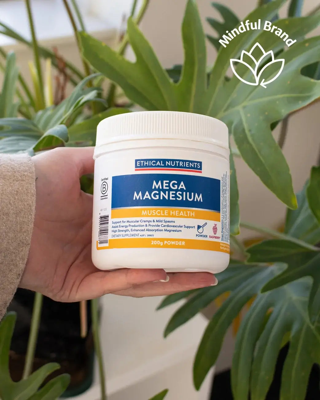 Hand holding a container of Ethical Nutrients Mega Magnesium powder with plants in the background.