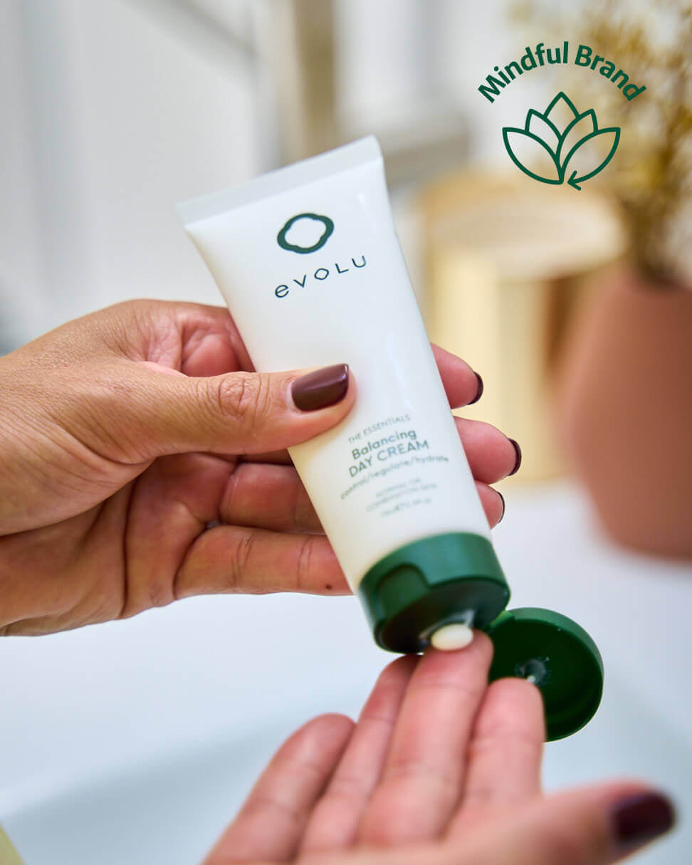 Hand holding a tube of Evolu day cream with 'Mindful Brand' logo in the background.