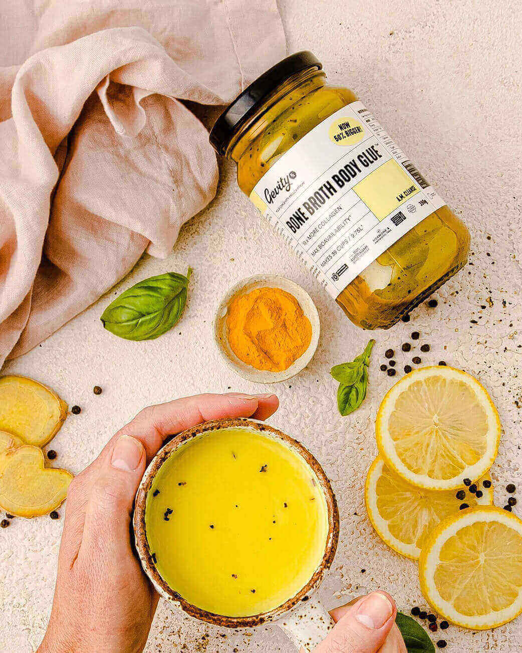 Bowl of yellow soup with a jar labeled 'Body Glue' on a textured surface with lemons and basil.