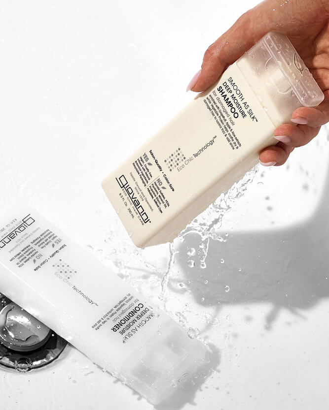 Hand holding a bottle of DHC shampoo with water splashes on a white background