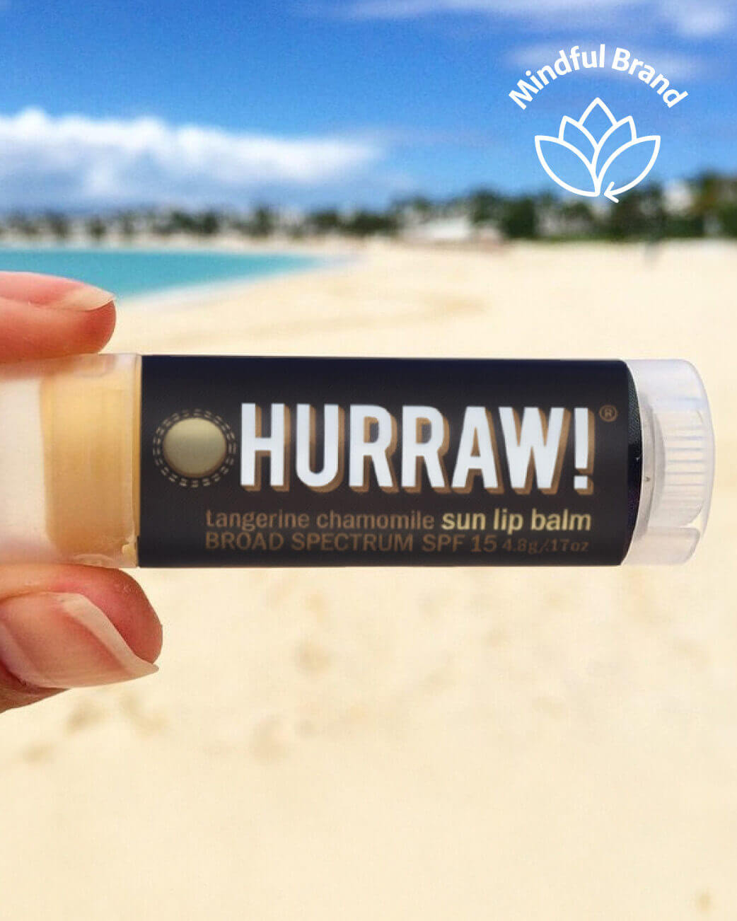 Hurraw! sun lip balm held in hand with beach background.
