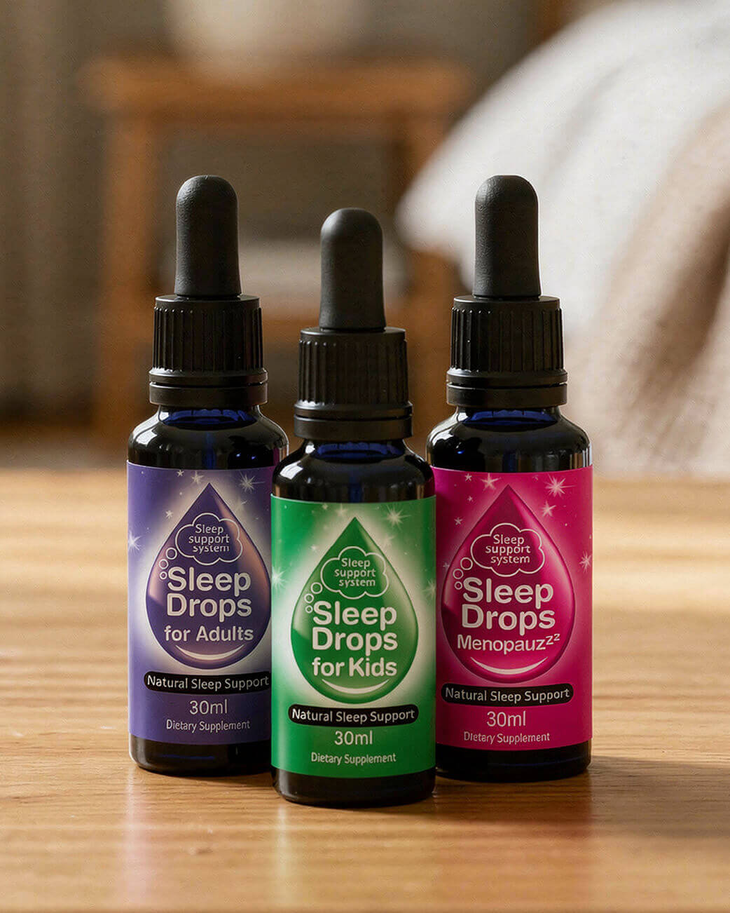 Three bottles of Sleep Drops on a wooden surface with a blurred background.