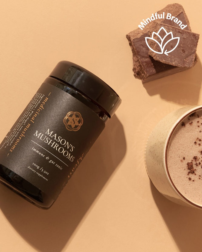 SuperFeast Mason's mushrooms supplement bottle laid on its side on a cream surface with a fluffy latte and chocolate next to it.