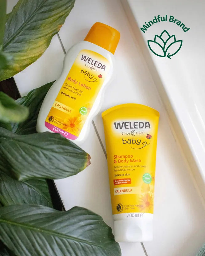 Weleda baby body lotion and shampoo & body wash products arranged on a white surface with green leaves. A 'Mindful Brand' logo is visible in the top right corner.