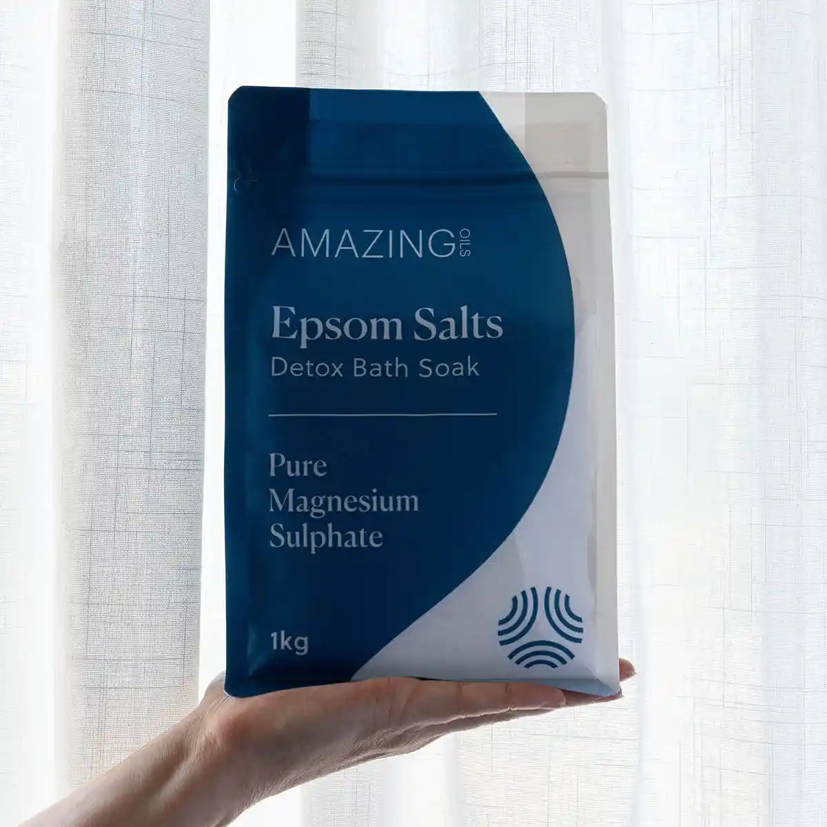 Bag of Amazing Epsom Salts Detox Bath Soak held in front of a white curtain